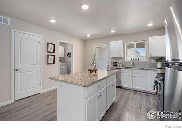 4216 Yellowbells Dr, Evans, CO 80620 - kitchen with appliances with stainless steel finishes, washer / clothes dryer, light wood-style flooring, a kitchen island, and recessed lighting