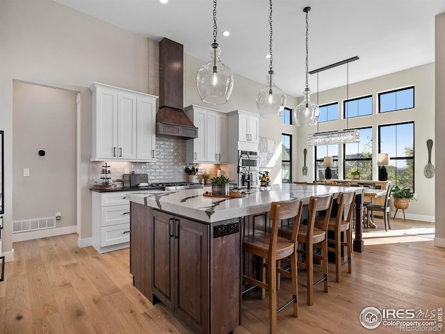 1255 Eliza Ave, Berthoud, CO 80513 - kitchen featuring custom range hood, a towering ceiling, white cabinets, a kitchen island with sink, and a kitchen bar