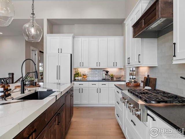 1255 Eliza Ave, Berthoud, CO 80513 - kitchen with custom exhaust hood, stainless steel gas cooktop, pendant lighting, white cabinets, and tasteful backsplash