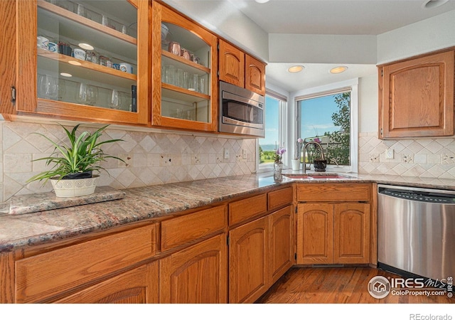 4615 Kitchell Way, Fort Collins, CO 80524 - kitchen with stainless steel appliances, dark wood-style floors, light stone countertops, brown cabinetry, and glass insert cabinets
