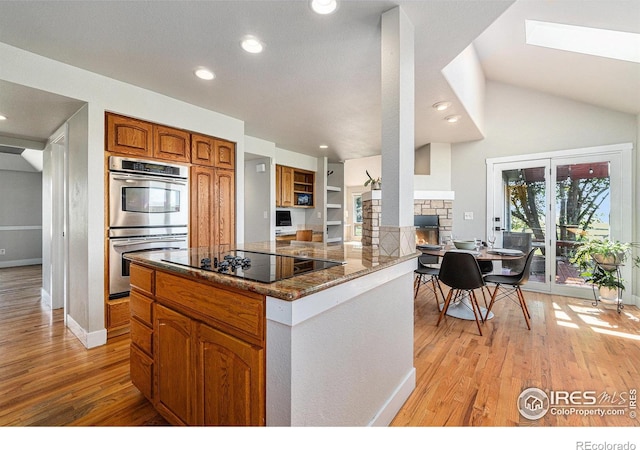 4615 Kitchell Way, Fort Collins, CO 80524 - kitchen with double oven, black electric stovetop, light wood-type flooring, brown cabinetry, and dark stone counters