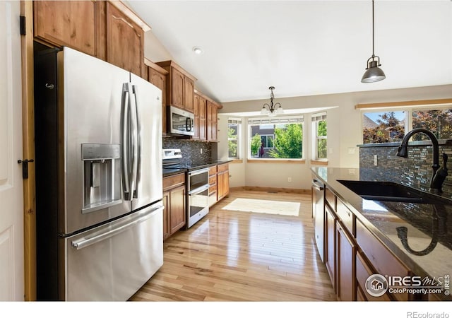 333 Braveheart Ln, Johnstown, CO 80534 - kitchen featuring appliances with stainless steel finishes, light wood-style floors, tasteful backsplash, vaulted ceiling, and pendant lighting