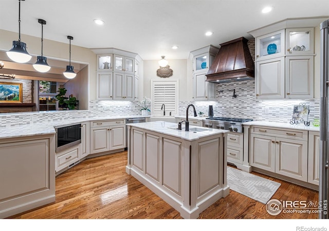 3000 E Cedar Ave Unit 2, Denver, CO 80209 - kitchen with custom range hood, appliances with stainless steel finishes, decorative backsplash, light wood finished floors, and glass insert cabinets