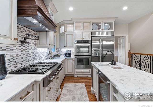 3000 E Cedar Ave Unit 2, Denver, CO 80209 - kitchen featuring appliances with stainless steel finishes, wall chimney range hood, dark wood-style flooring, light stone counters, and glass insert cabinets