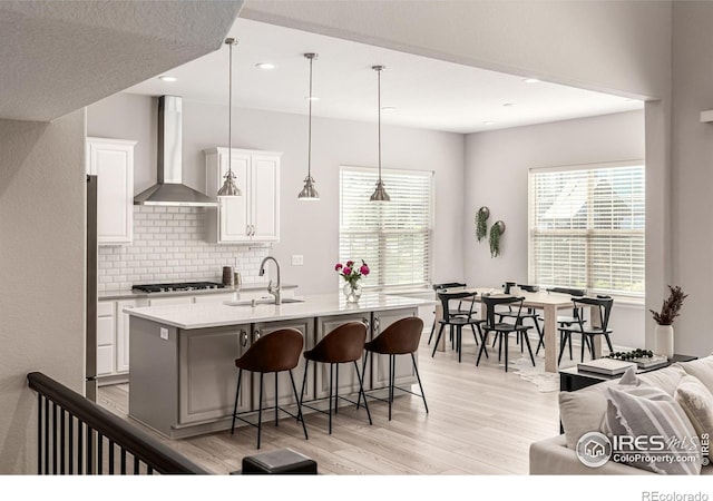 1389 Lyons Ln, Erie, CO 80516 - kitchen featuring wall chimney range hood, gas cooktop, light wood finished floors, a breakfast bar, and decorative backsplash