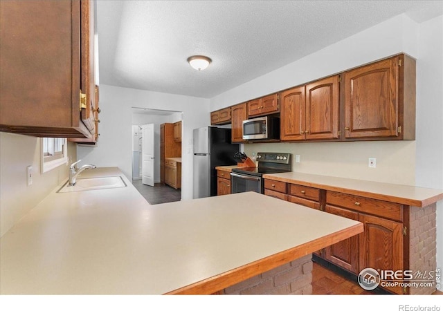 3400 Erving Ct, Berthoud, CO 80513 - kitchen with appliances with stainless steel finishes, a peninsula, light countertops, brown cabinets, and a textured ceiling