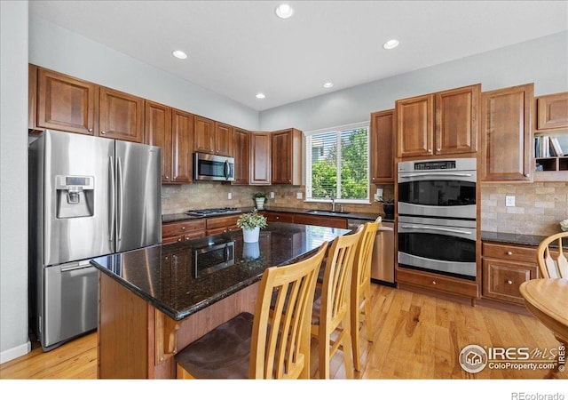 2707 Pochard Ct, Johnstown, CO 80534 - kitchen featuring appliances with stainless steel finishes, light wood-type flooring, a breakfast bar area, backsplash, and a center island