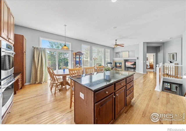 2707 Pochard Ct, Johnstown, CO 80534 - kitchen with light wood-type flooring, stainless steel double oven, a breakfast bar area, a glass covered fireplace, and a center island