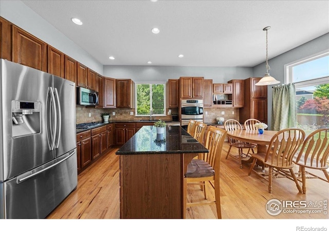 2707 Pochard Ct, Johnstown, CO 80534 - kitchen featuring appliances with stainless steel finishes, light wood-style floors, a kitchen island, decorative light fixtures, and backsplash