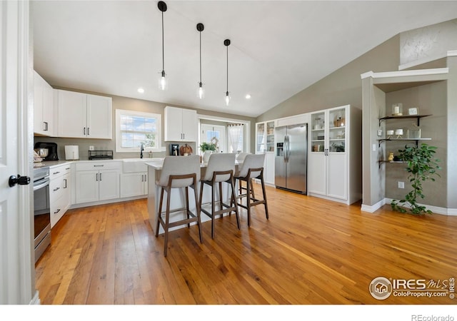 34427 County Rd W, Hillrose, CO 80733 - kitchen featuring stainless steel appliances, light wood-type flooring, lofted ceiling, a kitchen bar, and light countertops