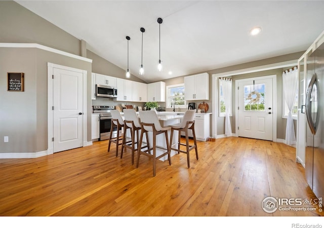 34427 County Rd W, Hillrose, CO 80733 - kitchen featuring appliances with stainless steel finishes, vaulted ceiling, a breakfast bar, light wood finished floors, and white cabinetry