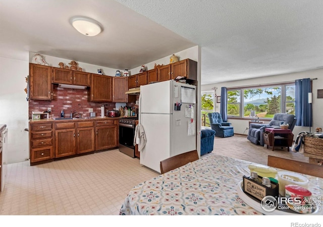 2110 Charro Ave, Longmont, CO 80504 - kitchen with freestanding refrigerator, stainless steel stove, open floor plan, brown cabinetry, and a textured ceiling