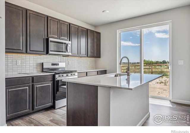 850 Mesic Ln, Windsor, CO 80550 - kitchen with appliances with stainless steel finishes, decorative backsplash, light wood-style flooring, dark brown cabinets, and a kitchen island with sink