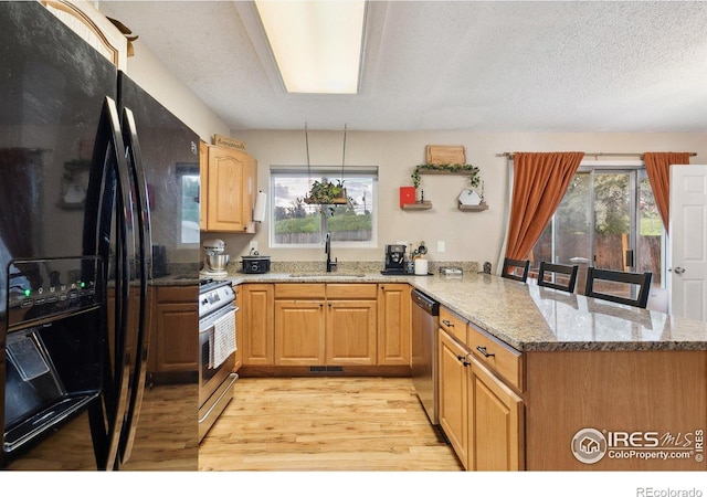 1607 Rushmore Dr, Colorado Springs, CO 80910 - kitchen featuring stainless steel appliances, a peninsula, light wood-type flooring, light stone counters, and a textured ceiling