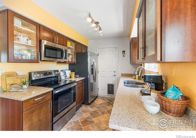 109 Sunflower Dr, Windsor, CO 80550 - kitchen with appliances with stainless steel finishes, dark stone finish flooring, glass insert cabinets, brown cabinetry, and light stone countertops