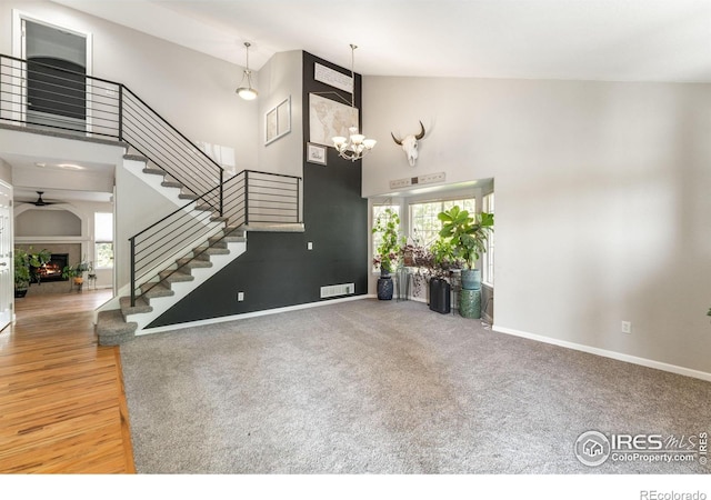 232 Ricker Ln, Johnstown, CO 80534 - unfurnished living room with high vaulted ceiling, stairway, a ceiling fan, a warm lit fireplace, and a chandelier
