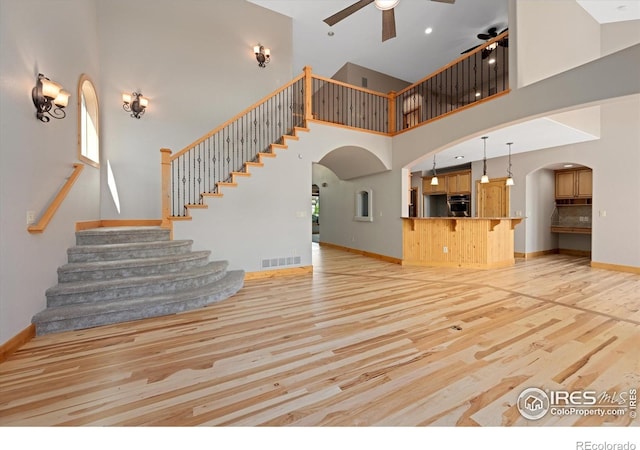 8416 Starfish Ct, Windsor, CO 80528 - unfurnished living room with arched walkways, ceiling fan, light wood-type flooring, a high ceiling, and stairs