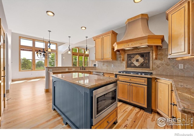 8416 Starfish Ct, Windsor, CO 80528 - kitchen featuring appliances with stainless steel finishes, premium range hood, light wood-type flooring, a peninsula, and a chandelier
