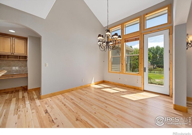 8416 Starfish Ct, Windsor, CO 80528 - unfurnished dining area featuring a chandelier, light wood-type flooring, arched walkways, and high vaulted ceiling
