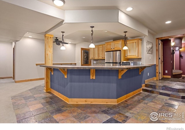8416 Starfish Ct, Windsor, CO 80528 - kitchen featuring appliances with stainless steel finishes, stone tile floors, light brown cabinetry, a kitchen bar, and a peninsula