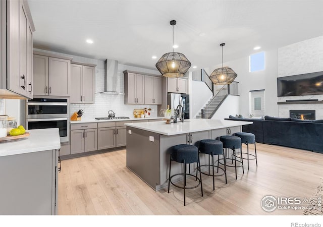 5056 Blanchette St, Timnath, CO 80547 - kitchen with wall chimney exhaust hood, gray cabinets, appliances with stainless steel finishes, a kitchen breakfast bar, and light wood-style floors