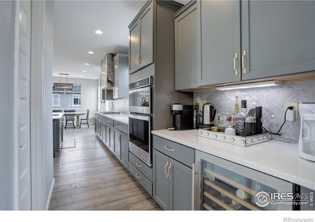 12917 Fox St, Westminster, CO 80234 - kitchen with stainless steel double oven, wine cooler, light wood-type flooring, gray cabinetry, and backsplash