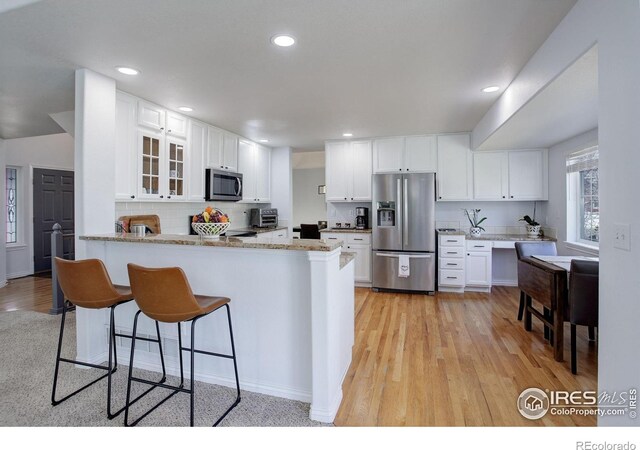 2547 Concord Cir, Lafayette, CO 80026 - kitchen featuring appliances with stainless steel finishes, a peninsula, glass insert cabinets, light wood finished floors, and a breakfast bar