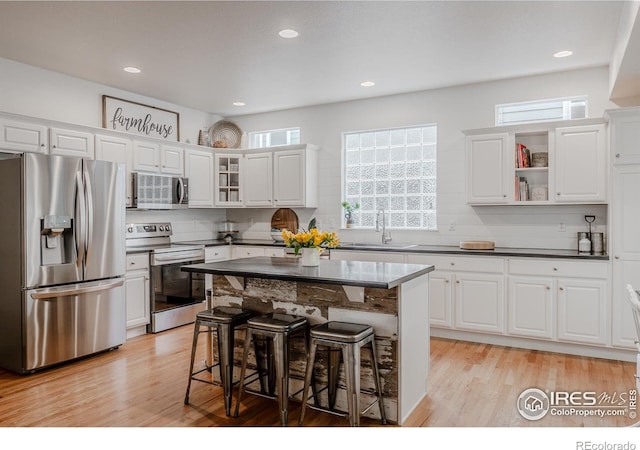 8367 Devinney St, Arvada, CO 80005 - kitchen featuring appliances with stainless steel finishes, dark countertops, a kitchen breakfast bar, tasteful backsplash, and light wood-style floors