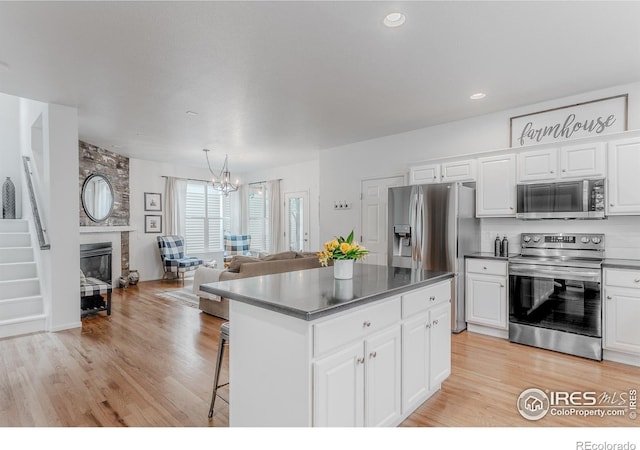 8367 Devinney St, Arvada, CO 80005 - kitchen with stainless steel appliances, a chandelier, a kitchen island, white cabinetry, and light wood-style flooring