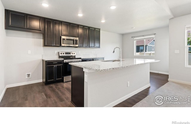 627 Overland Trl, Ault, CO 80610 - kitchen featuring stainless steel appliances, a kitchen island with sink, light stone counters, dark wood-style flooring, and recessed lighting
