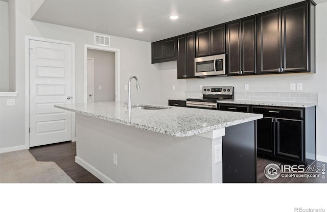 627 Overland Trl, Ault, CO 80610 - kitchen with appliances with stainless steel finishes, dark wood finished floors, a kitchen island with sink, recessed lighting, and light stone counters