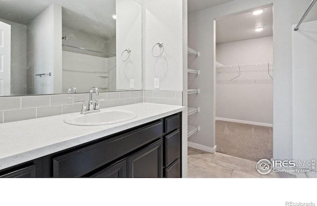 627 Overland Trl, Ault, CO 80610 - bathroom featuring vanity, a walk in closet, a shower, decorative backsplash, and tile patterned floors