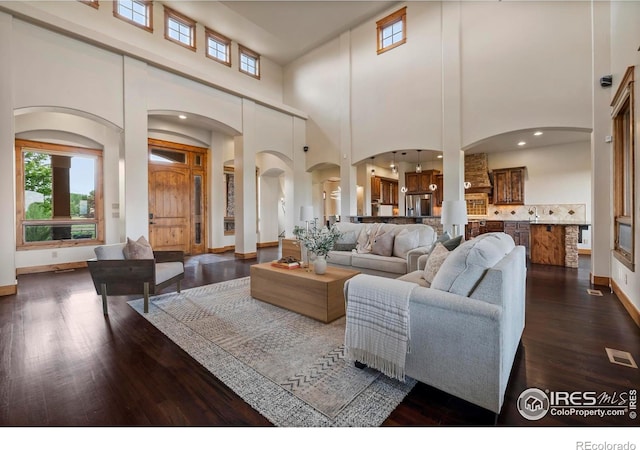 863 Riparian Way, Fort Collins, CO 80524 - living room featuring arched walkways, healthy amount of natural light, dark wood finished floors, a high ceiling, and decorative columns
