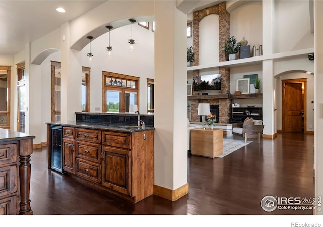 863 Riparian Way, Fort Collins, CO 80524 - kitchen featuring beverage cooler, arched walkways, dark wood-type flooring, a stone fireplace, and open floor plan
