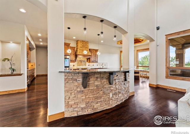 863 Riparian Way, Fort Collins, CO 80524 - kitchen featuring dark wood-style floors, arched walkways, custom exhaust hood, a breakfast bar area, and recessed lighting