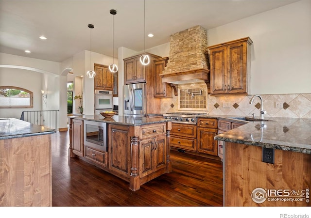863 Riparian Way, Fort Collins, CO 80524 - kitchen with stainless steel appliances, premium range hood, brown cabinetry, dark wood-style floors, and tasteful backsplash