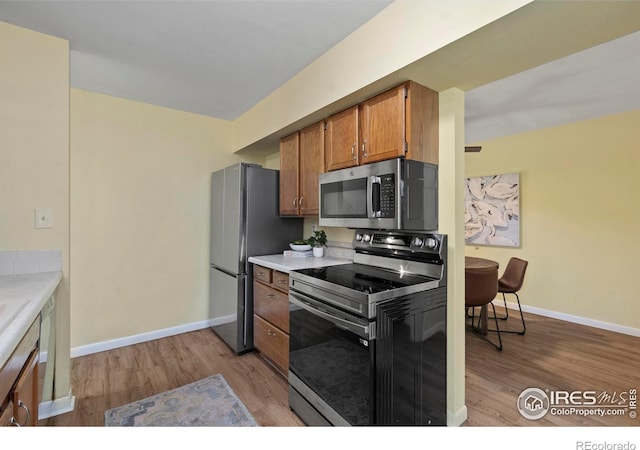 705 E Drake Rd Unit 40, Fort Collins, CO 80525 - kitchen with appliances with stainless steel finishes, brown cabinetry, light wood-type flooring, and light countertops