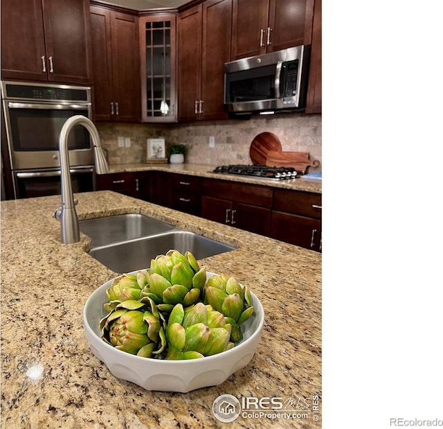 306 Baja Dr, Windsor, CO 80550 - kitchen featuring appliances with stainless steel finishes, glass insert cabinets, light stone counters, and backsplash