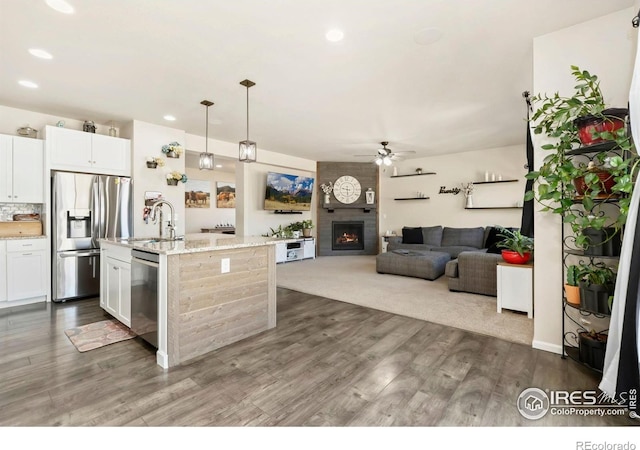 6504 Zimmerman Lake Rd, Timnath, CO 80547 - kitchen featuring stainless steel appliances, a ceiling fan, dark wood-type flooring, a large fireplace, and light stone counters