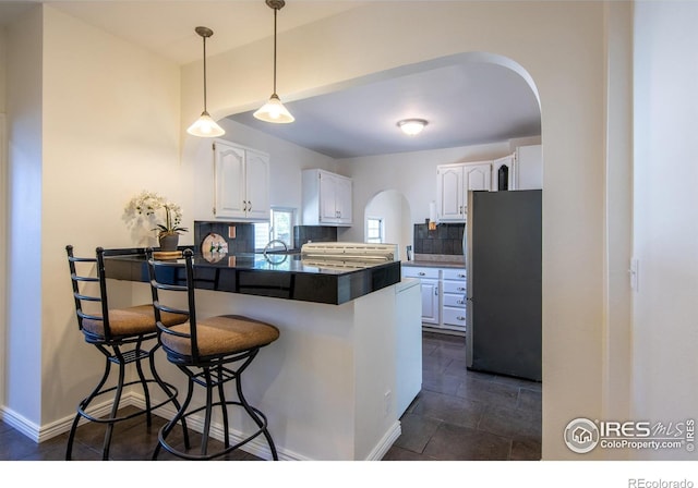 403 W Cannon St, Lafayette, CO 80026 - kitchen featuring freestanding refrigerator, a peninsula, dark countertops, arched walkways, and white cabinets