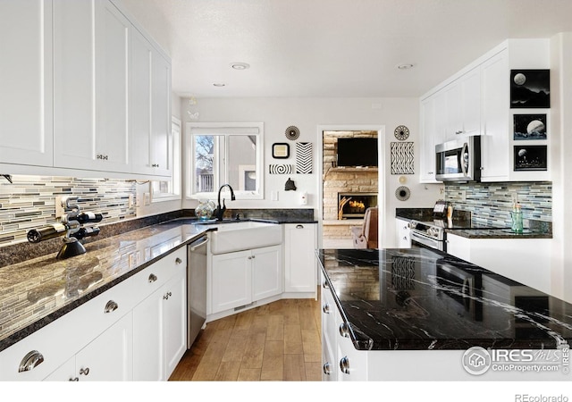 5072 Saint Andrews Dr, Loveland, CO 80537 - kitchen featuring stainless steel appliances, white cabinetry, light wood-style floors, backsplash, and dark stone counters