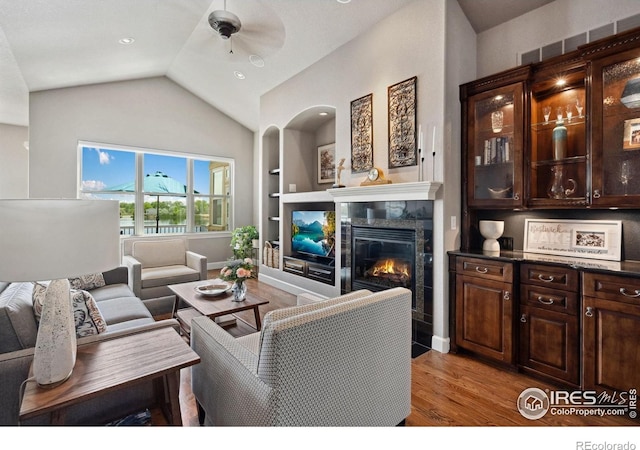 2055 Vineyard Dr, Windsor, CO 80550 - living room featuring built in shelves, a tiled fireplace, ceiling fan, light wood-type flooring, and vaulted ceiling
