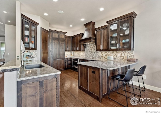 2055 Vineyard Dr, Windsor, CO 80550 - kitchen with custom range hood, a peninsula, dark brown cabinets, light stone countertops, and recessed lighting