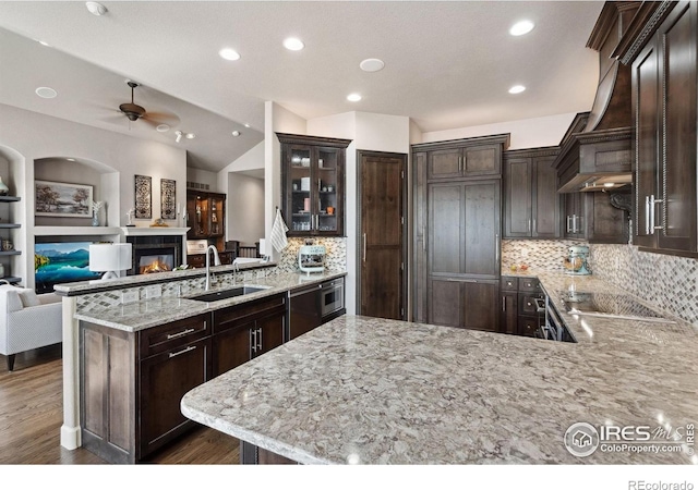 2055 Vineyard Dr, Windsor, CO 80550 - kitchen featuring a peninsula, dark brown cabinets, a glass covered fireplace, ceiling fan, and light stone countertops