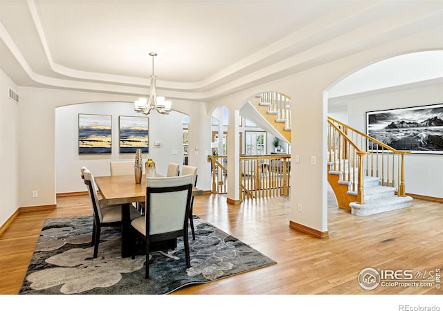 14601 Akron St, Brighton, CO 80602 - dining space featuring wood finished floors, a chandelier, a tray ceiling, stairway, and arched walkways