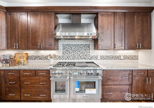 14601 Akron St, Brighton, CO 80602 - kitchen featuring range with two ovens, wall chimney range hood, decorative backsplash, and light stone countertops