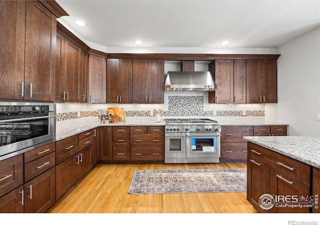 14601 Akron St, Brighton, CO 80602 - kitchen featuring appliances with stainless steel finishes, wall chimney range hood, light wood finished floors, decorative backsplash, and recessed lighting