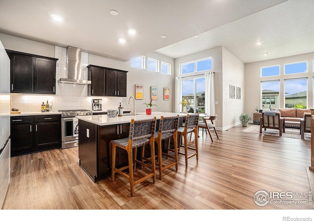 2716 San Cristobal Ct, Timnath, CO 80547 - kitchen featuring wall chimney range hood, high end stove, a breakfast bar, a kitchen island with sink, and light wood-style flooring
