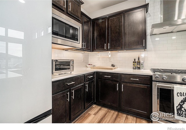 2716 San Cristobal Ct, Timnath, CO 80547 - kitchen featuring wall chimney range hood, appliances with stainless steel finishes, light countertops, light wood-style flooring, and tasteful backsplash