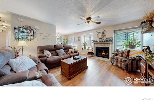 4557 W Pioneer Ln, Greeley, CO 80634 - living room with a textured ceiling, light wood-style flooring, a ceiling fan, a chandelier, and a tile fireplace